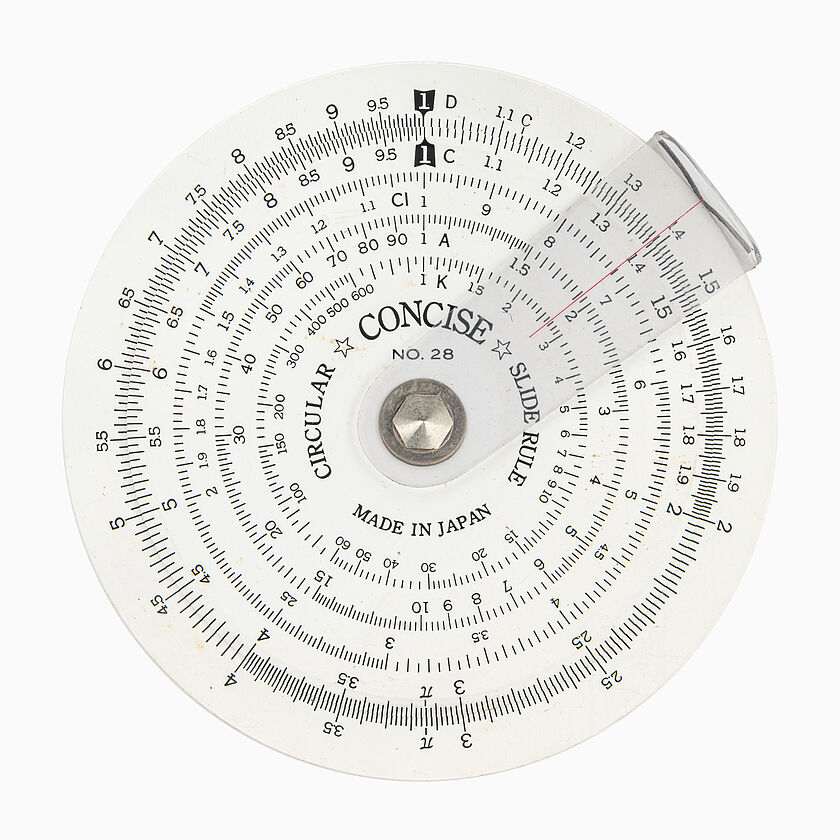 Weiße, runde Scheibe mit in kreisrichtung verschiebbarer Plastik Lasche (roter Strich radial). Mehrere Zeilen mit Skalen und Zahlen kreisförmig angeordnet.