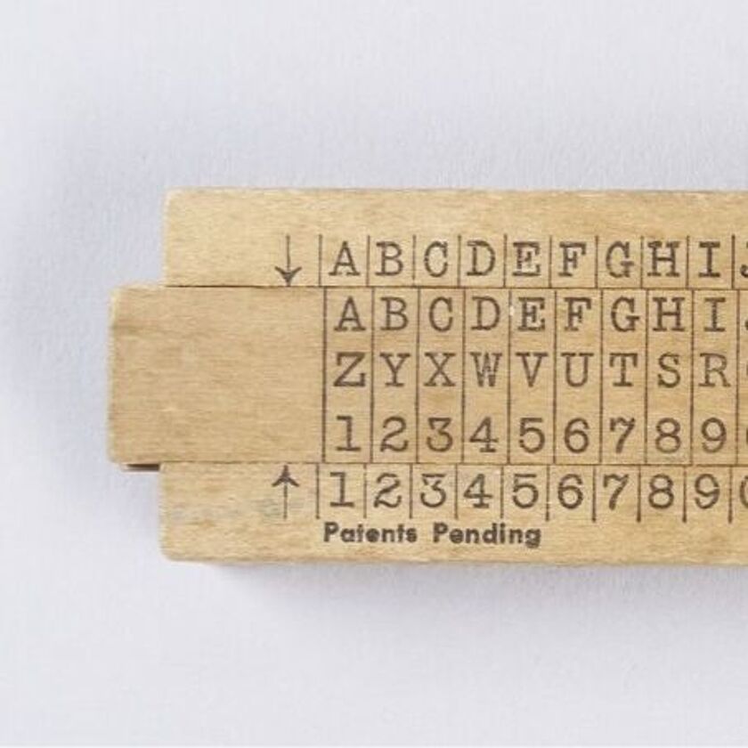 Holzschieber. Fest oben Alphabet zweifach, unten wiederholte Zahlenfolge 0 bis 9. Mittig verschiebbar drei Zeilen: Alphabet, Alphabet rückläufig, Zahlenfolge 0 bis 9