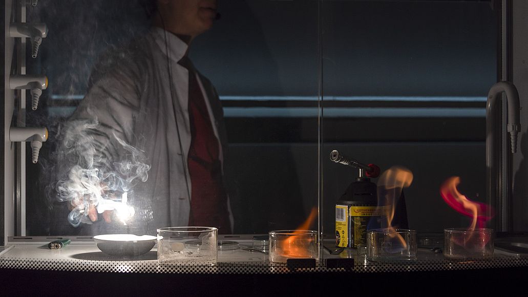 Eine Mitarbeiterin der Ausstellung Chemie zündet im Labor Salze an und eine weiße Flamme sticht empor.