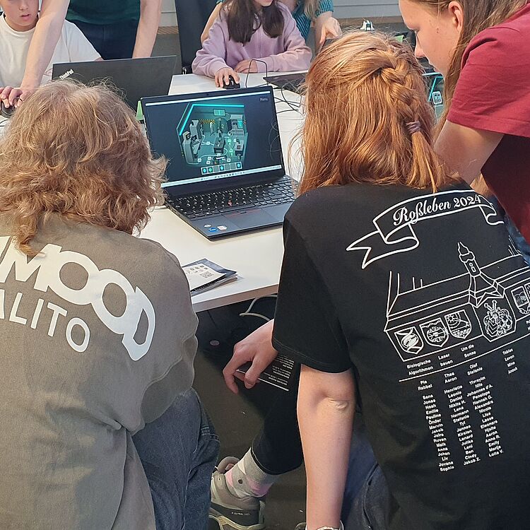 Eine Gruppe von Menschen blickt auf ein Computerspiel, in dem ein Quantenlabor dargestellt ist.