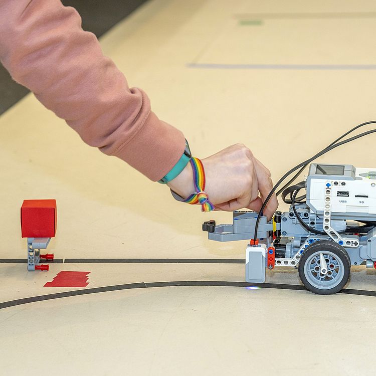 Hand aktiviert Roboter mit Sensoren des TUMLabs, der einen kleinen, roten Karton aufheben soll.
