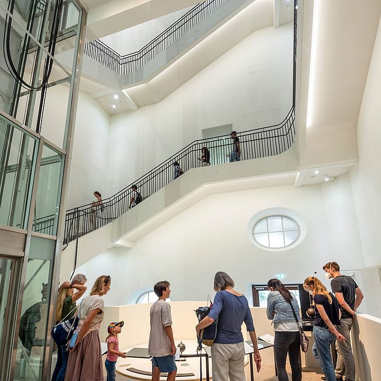 Das Foucault'sche Pendel Besucher stehen im Museum vor einem Foucault’schen Pendel und beobachten dessen gleichmäßige Schwingung.