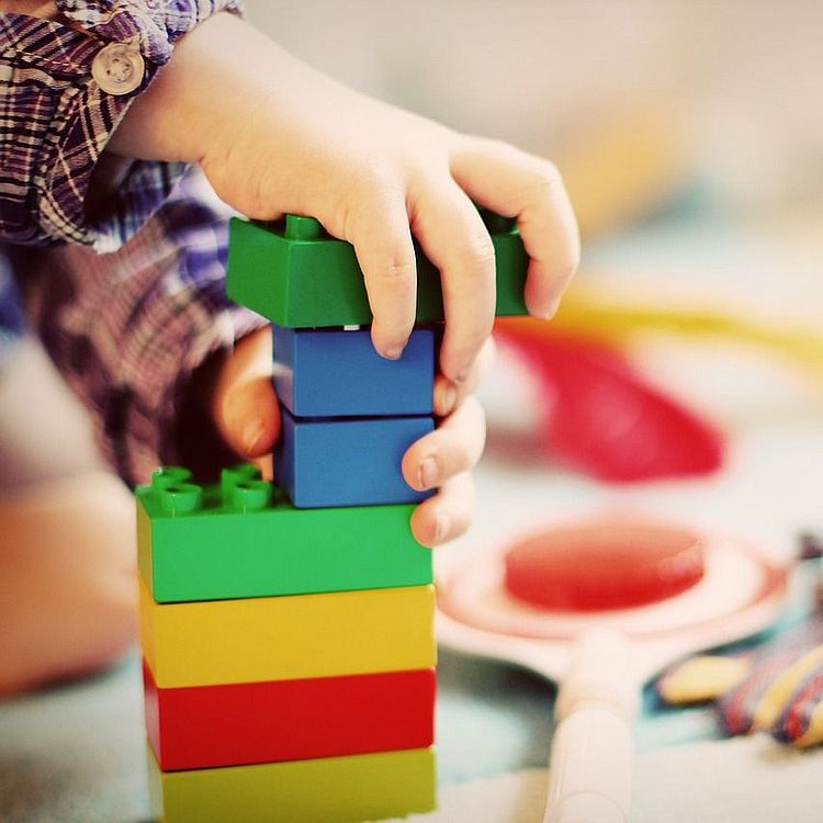 Kleinkind baut mit verschieden farbigen Lego Duplo Steinen einen Turm.