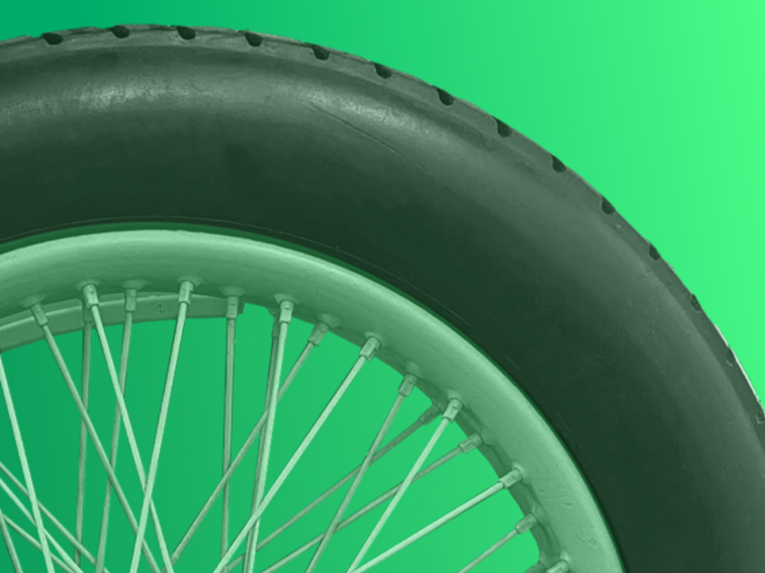 Nahaufnahme eines Fahrradreifens und einer Speichenfelge vor grünem Hintergrund; schwarze Gummibereifung, hellgrüne Felge und zahlreiche Metall-Speichen sichtbar.