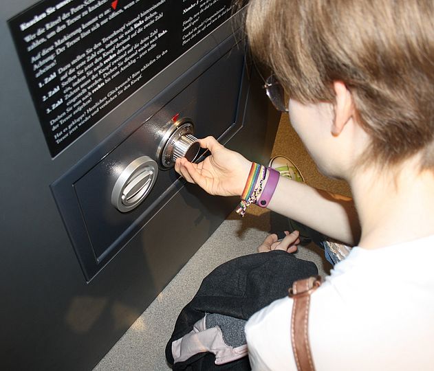 Schülerin versucht mit Hilfe eines Codes den Safe in der Ausstellung "Bild Schift Codes" zu knacken.