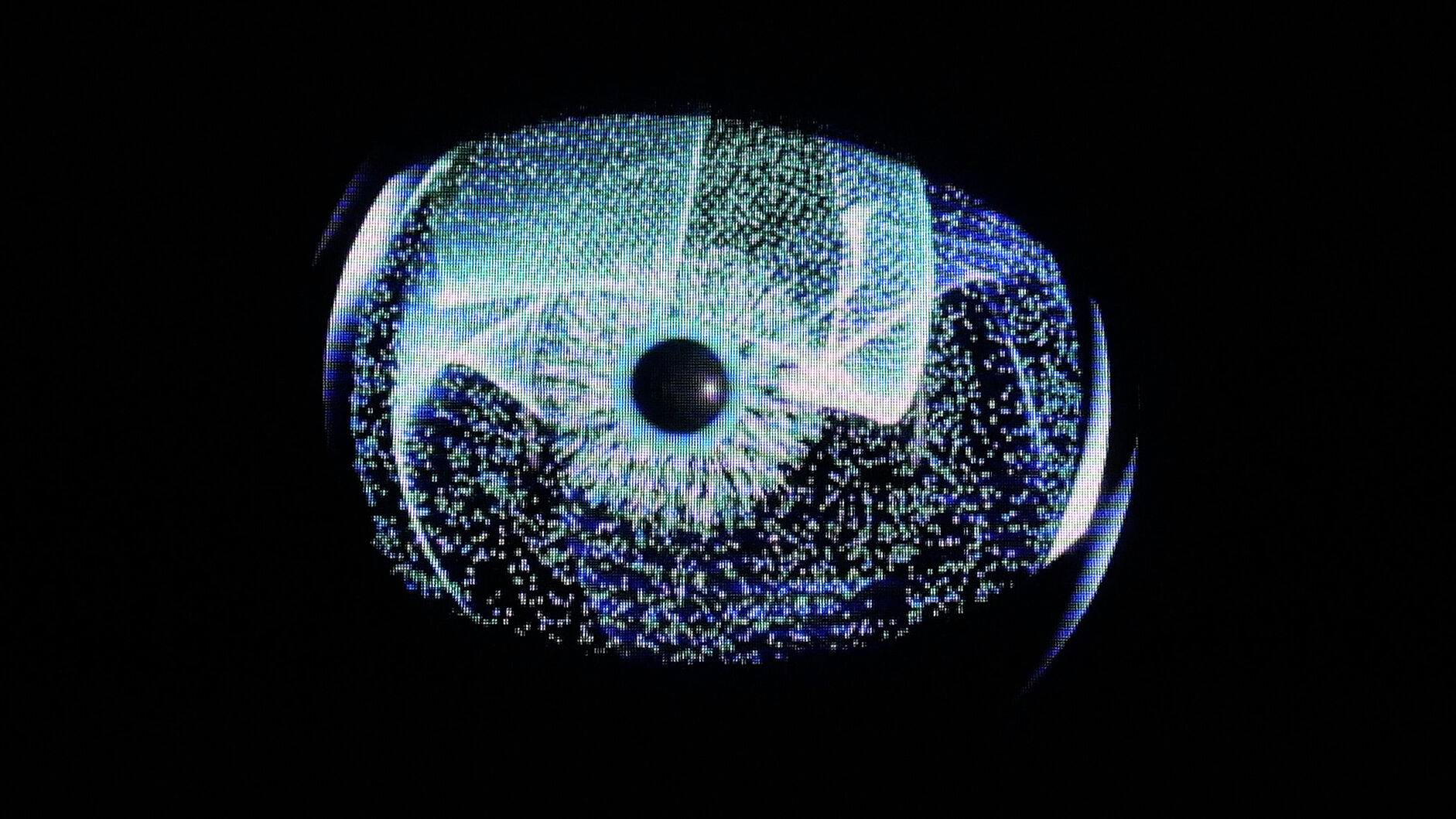 Nahaufnahme einer leuchtenden, digitalen Iris-ähnlichen Grafik: zentrale dunkle Pupille, radial strahlende blaue und grüne Pixelpunkte und Linien auf schwarzem Hintergrund, erinnert an ein Auge oder ein abstraktes Datavisualisierungs-Interface.