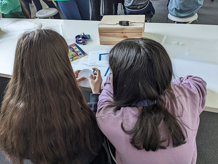 Kinder beim Versuch, ein Zahlenschloss mit einer Transkriptions-Scheibe zu öffnen.