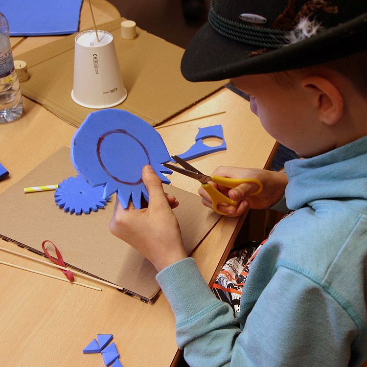 Junge schneidet aus blauem, dickem Moosgummi ein Zahnrad aus.