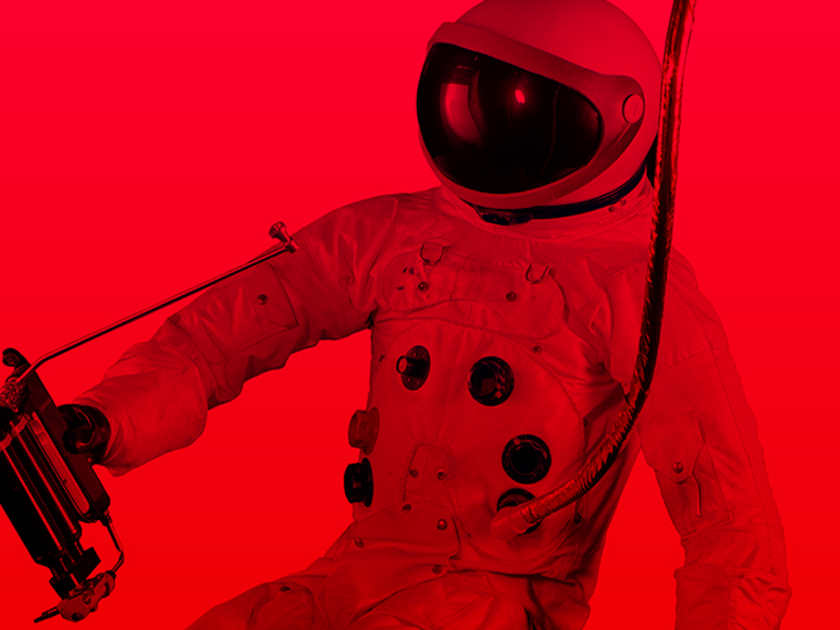 Ein Astronaut in einem klassischen Raumanzug mit rundem, dunklem Visier, mehreren runden Anschlussventilen auf der Brust und einem dicken Versorgungsschlauch, vor einem einfarbigen kräftigen roten Hintergrund.
