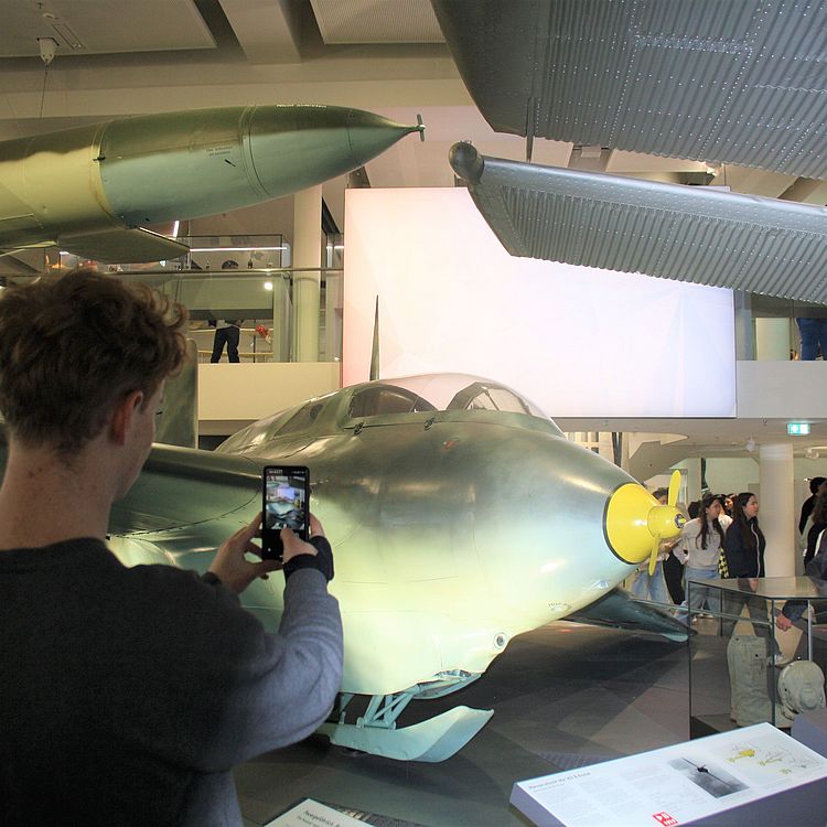 Schüler mit Smartphone, vor dem Flugzeug Messerschmitt Me 163 in der Ausstellung "Historische Luftfahrt".